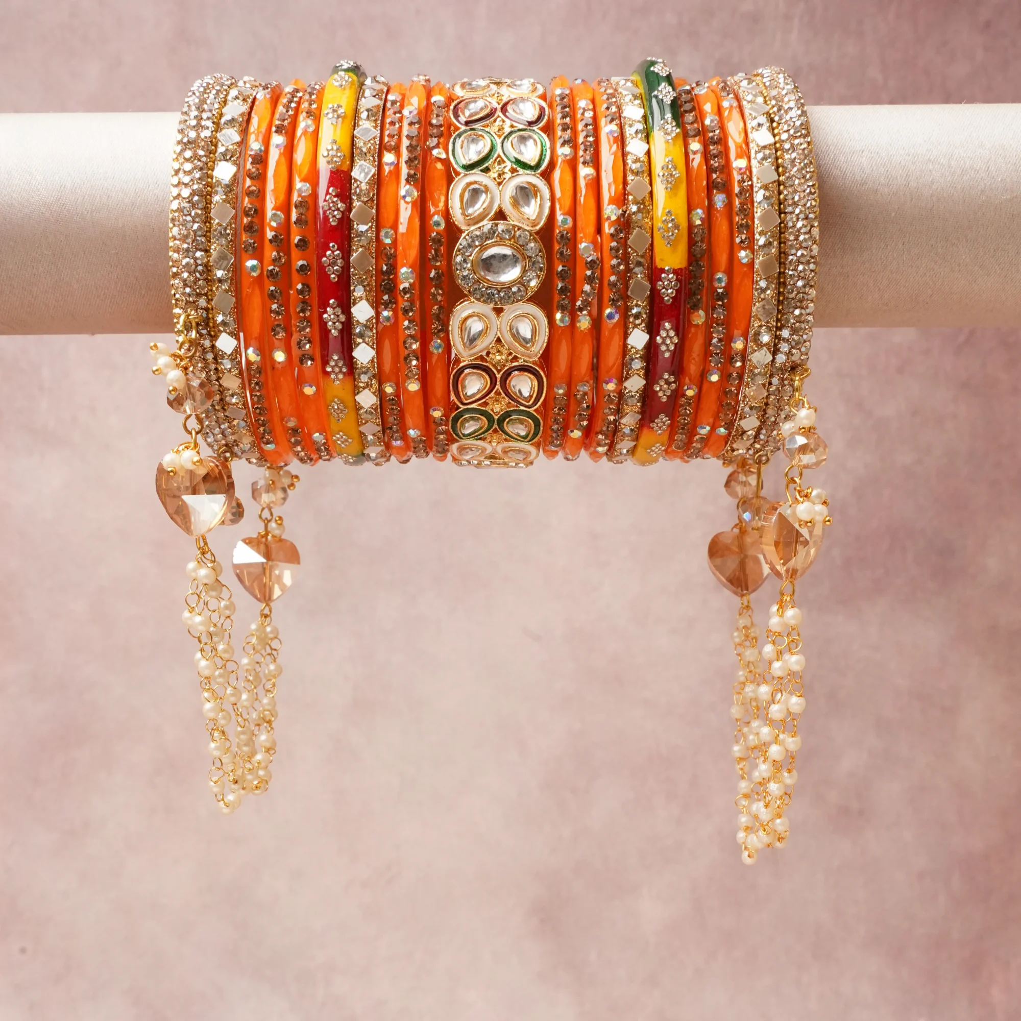 A commanding Tangerine Orange anchors this beautiful set, enriched with accents of Opulent White, Forest Green, Maroon, Golden Yellow, Brilliant Clear, Champagne Beige that add depth and dimension.

Featuring a striking composition of Lacquered Metal (Bangles), Glass (Bangles), Kundan (Polki-style Stone Setting), Zirconia/Glass Crystals, Gold-Plated Base Metal, Silver-Toned Base Metal, Enamel/Meenakari, Faux Pearls, Faceted Glass Beads, this set carries intricate craftsmanship and strong presence. Grand in form, it is created for moments that deserve to be marked.